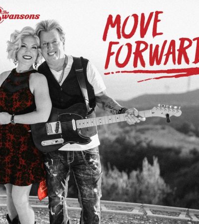 woman in red dress standing with man wearing white tshirt and black vest holding electric guitar